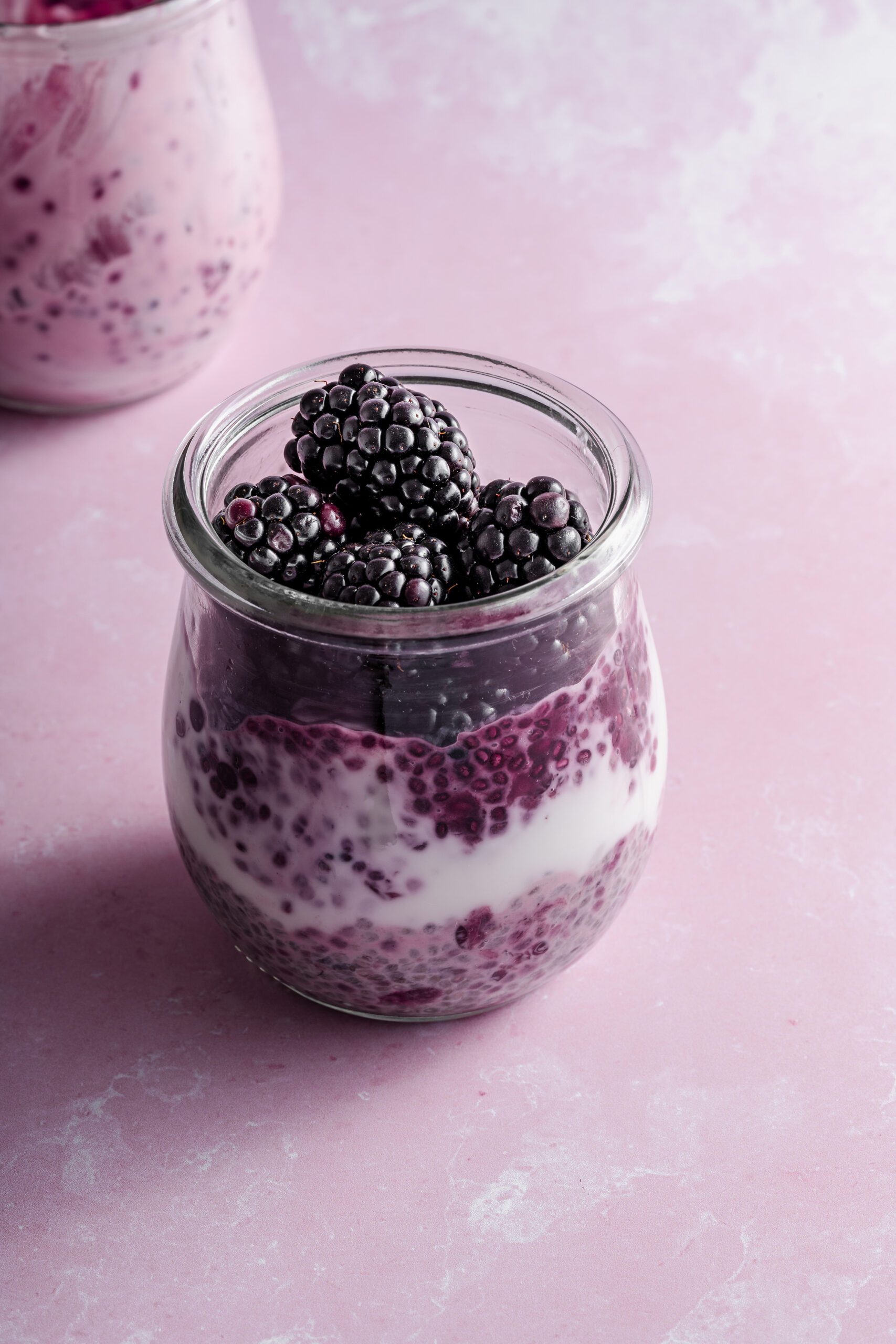 Glass jar filled with creamy yogurt, topped with fresh blackberries.